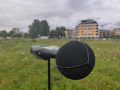 Zvukomer s veternou penou v popredí, v pozadí rozostavaná bytová budova s žeriavom
