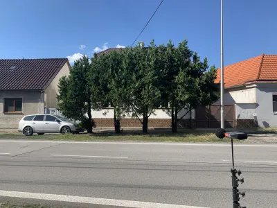 Zvukomer na statíve na ulici oproti rodinnému domu obklopenému stromami