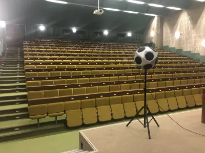 Guľový reproduktor na statíve v prázdnej stupňovitej sále s radmi žltých sedadiel