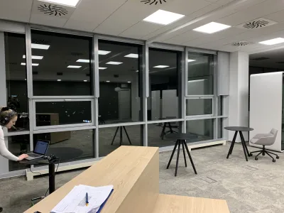 Žena pracuje na notebooku pri okne otvorenej kancelárie, večerný záber administratívnej budovy.