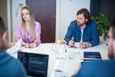 Členovia tímu diskutujú nad podkladmi pri stole počas pracovného stretnutia k certifikácii budovy.