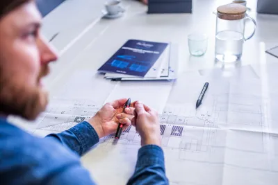 A man reviews construction drawings and technical documents on a table while preparing a project.