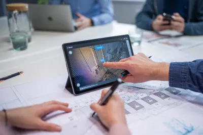 A team reviews a 3D building model on a tablet alongside paper drawings on the table.