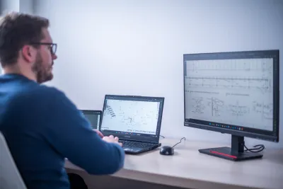 A man works on a technical construction drawing across two monitors in an office.
