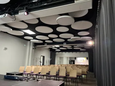 A hall with round acoustic ceiling panels and rows of seating, an example of a completed acoustic installation.