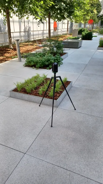 Detailný záber 3D skenera Leica na statíve medzi zeleňou.
