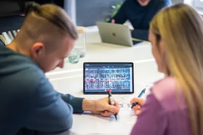 Dvaja pracovníci si prezerajú 3D model interiéru s bodmi skenovania na tablete.