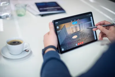 Ruka drží tablet s 3D skenom vonkajších klimatizačných jednotiek na streche.